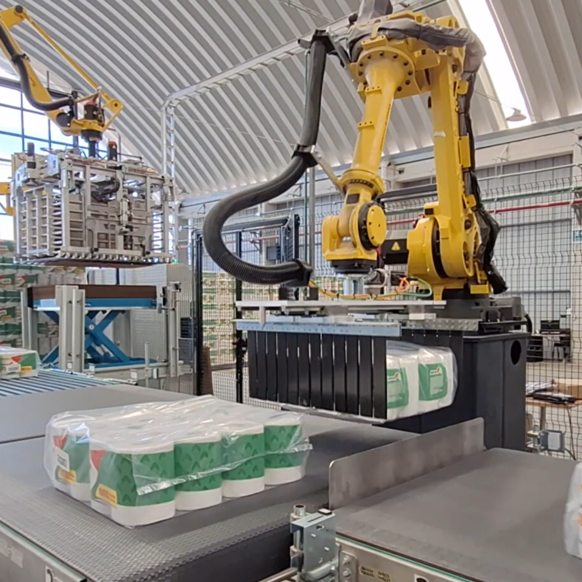 braccio robotico antropomorfo che manipola rotoli di carta su un nastro trasportatore per la preparazione dello strato