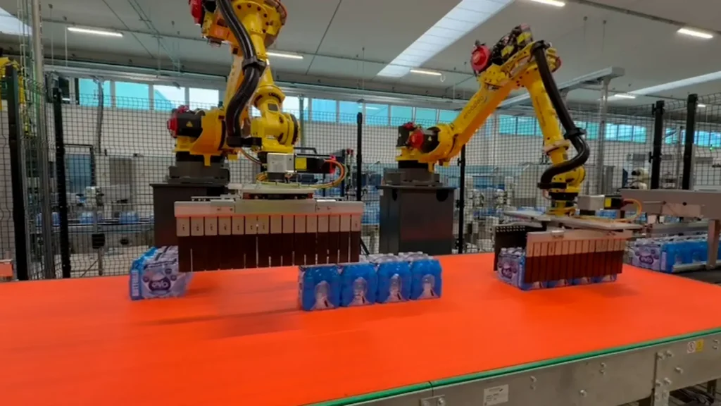 Due robot antropomorfi gialli del sistema Ercopac Nexus in produzione presso lo stabilimento Fonti Alta Valle Po, con bottiglie d'acqua in fase di pallettizzazione su nastro trasportatore arancione