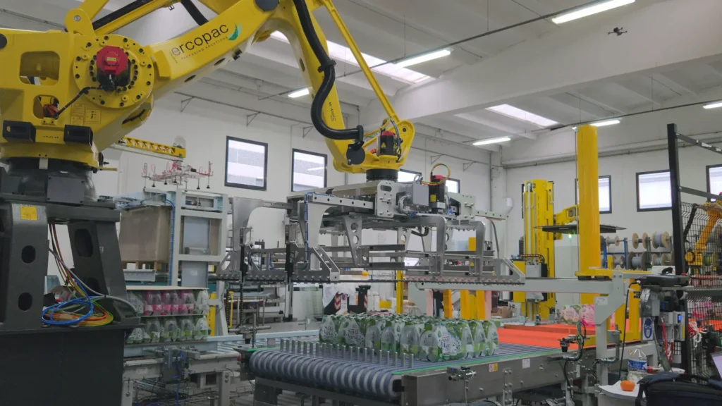 An Ercopac robot with an anthropomorphic arm handling bottles of mineral water on an automated end-of-line assembly line at the Capès Dolé plant, with a column-type case packer in the background