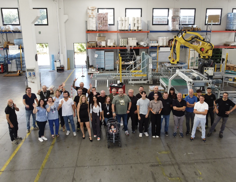 Team Ercopac al completo in un'area di produzione, con robot e macchinari sullo sfondo, a simboleggiare la crescita aziendale.