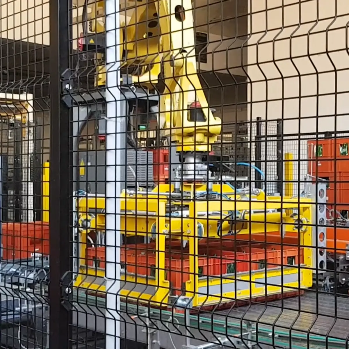 "Depallettizzatore robotizzato 'PANTHER', dotato di un braccio robotico con pinza di presa progettata per movimentare casse e contenitori. L'unità opera all'interno di un'area delimitata da una rete di protezione metallica per garantire la sicurezza durante le operazioni. Visibili anche componenti di supporto e linee di trasporto per l'automazione industriale."