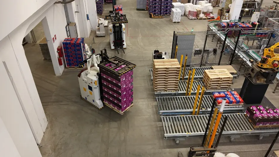 navetta agv per movimentazione pallet nel fine linea con scatole impilate su linea industriale automatizzata